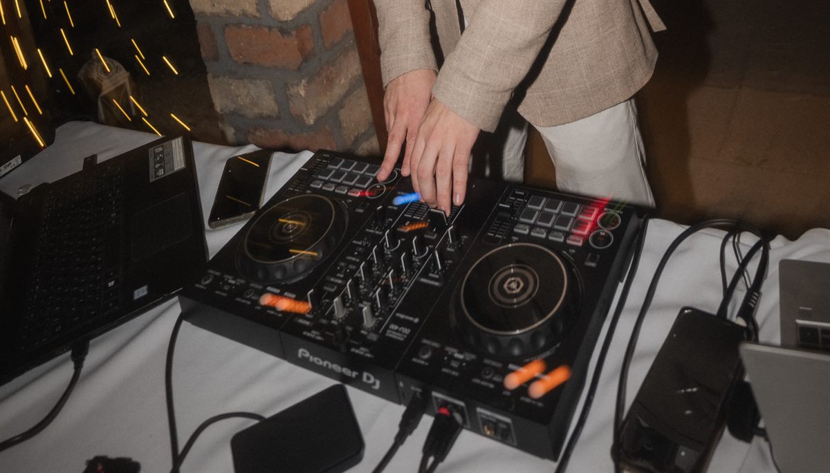 A DJ keze a Pioneer DJ keverőpulton, esküvői hangulatfényekkel a háttérben